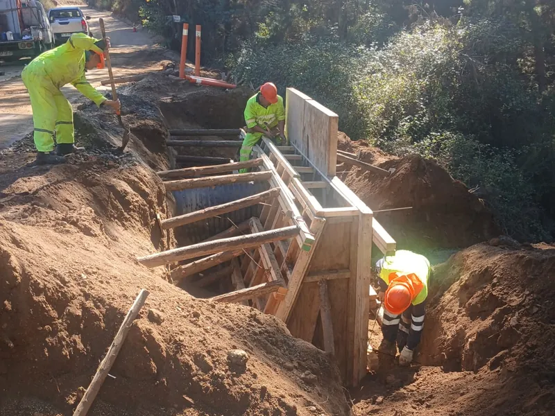 Obreros con ropa de alta visibilidad instalando la formaleta de madera de una alcantarilla de cajón en una excavación junto a un camino